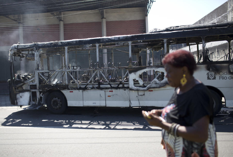 A woman walks past a bus allegedly set on fire by drug traffickers in the Bonsucesso neighborhood, Rio de Janeiro, Brazil, Monday, Aug. 20, 2018. Since February, the military has been in charge of security in the state of Rio de Janeiro, which is struggling to curb a spike in violence. (AP Photo/Silvia Izquierdo)