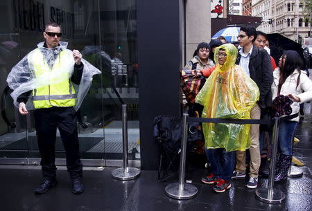 A security guard stands next to customers as they stand in the rain waiting to enter the Apple store during the official launch of the iPhone 6s in central Sydney, Australia, September 25, 2015. REUTERS/David Gray