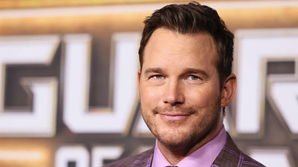 Chris Pratt soft smiles in a purple shirt and dark purple suit