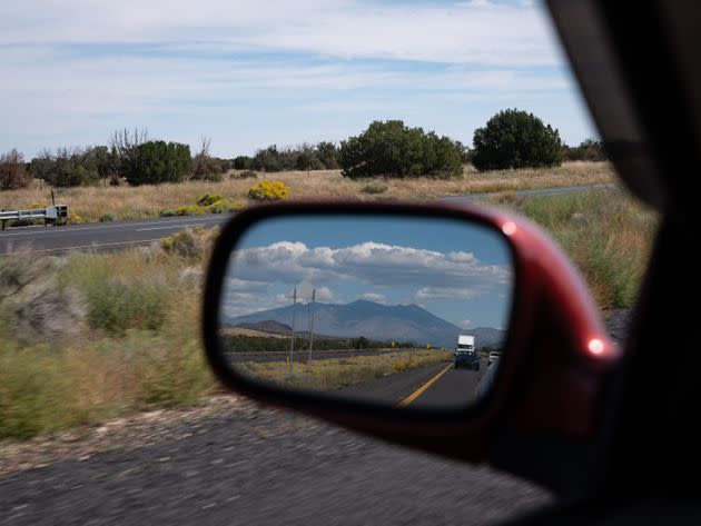 The San Francisco Peaks, mountains sacred to the Diné (Navajo) and other tribes, are reflected in the rearview mirror while traveling east from Flagstaff, Arizona, on Sept. 29, 2022. (Photo: Molly Peters for HuffPost)