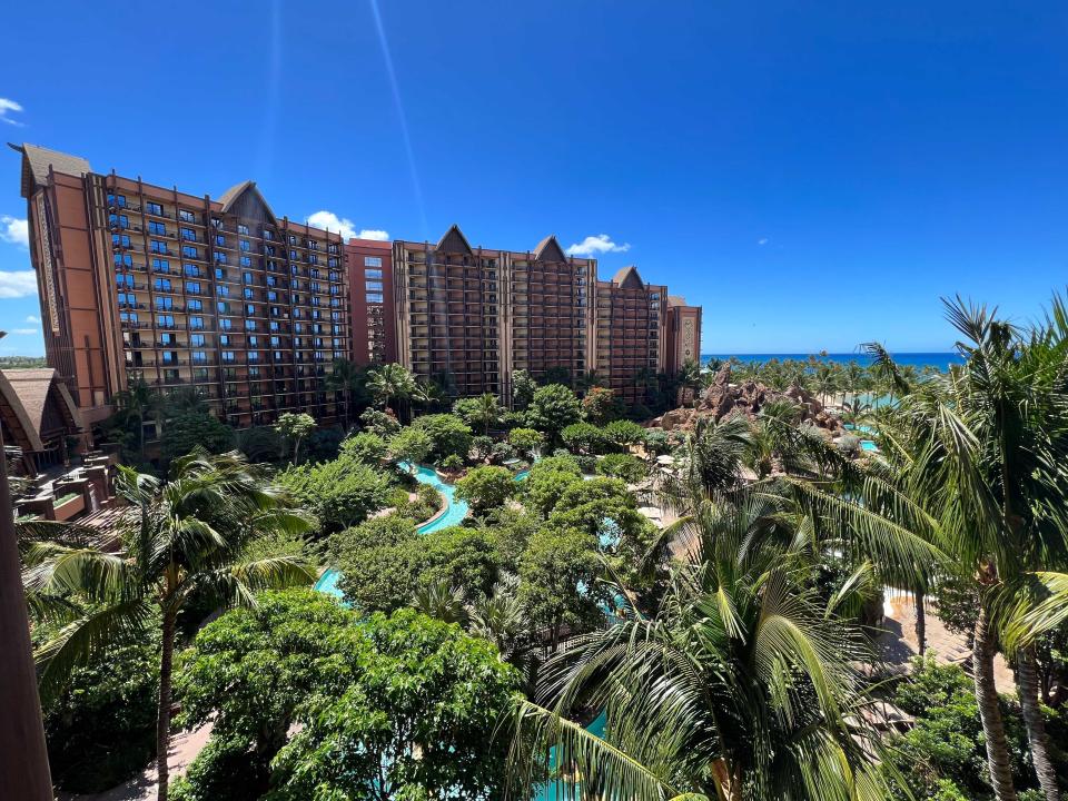 A view over the lazy river and hotel grounds including the hotel tower and beach in the distance at Aulani Disney resort.