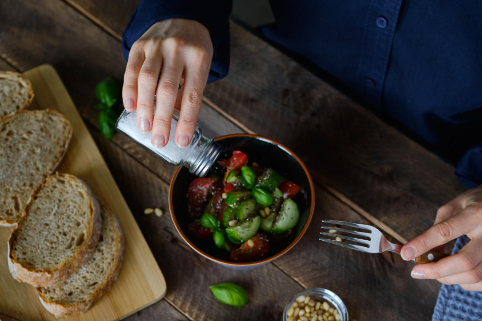 Vegetarian, vegan, and raw food. A girl or Woman Eats a Vegetable salad of tomatoes, cucumbers, nuts and seeds, Green Basil Leaves, and Salts It From a salt Shaker. Next To It Are Sliced Baguette Slices. The concept of Healthy eating, diet.