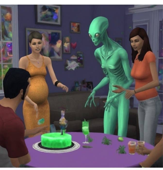 Two women and a man gathered around a table with a green alien, celebrating, in a Sims video game scenario