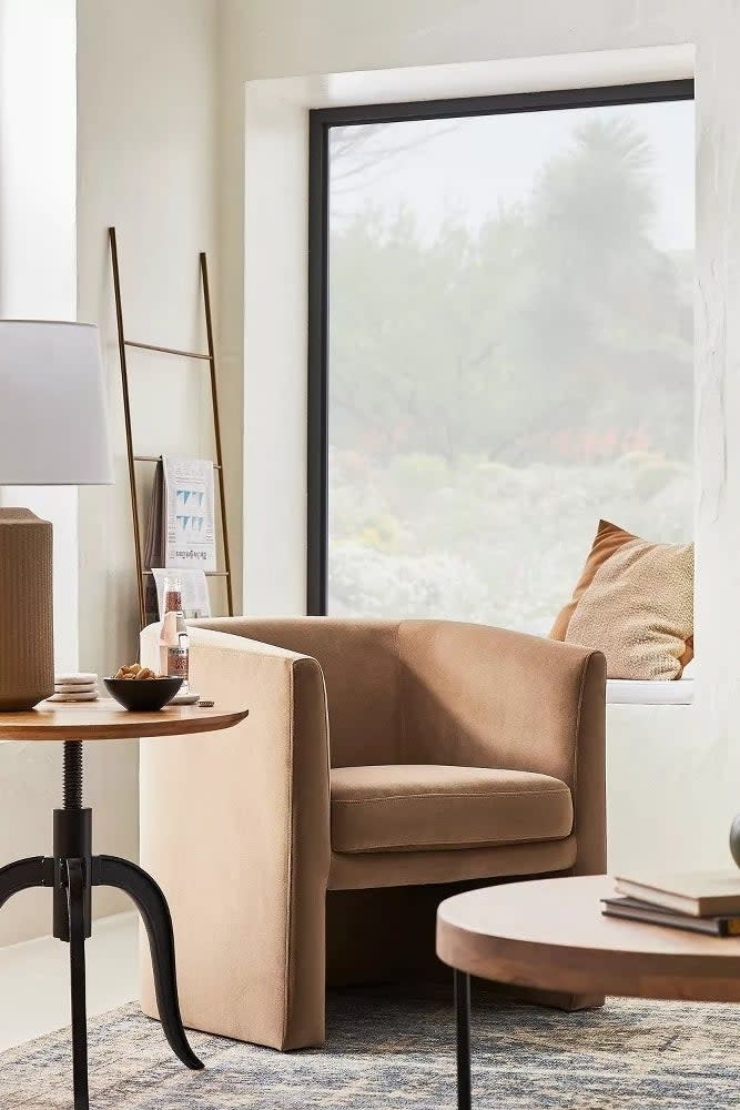 Cozy living room setup with brown velvet armchair, side table with lamp, bookshelves, and decorative items