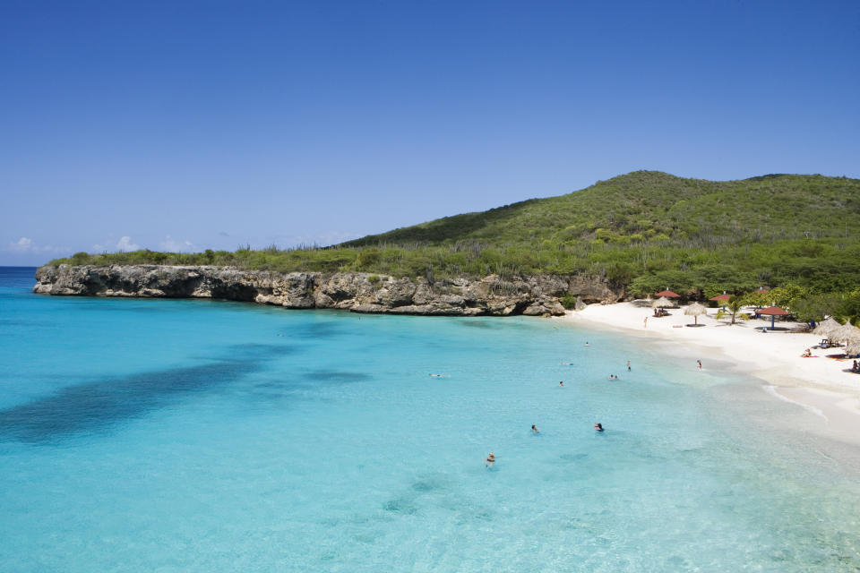 Beach with clear water, swimmers, and greenery-covered hills