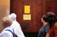 Tourists walk past signs pasted on a closed grand house entry in Palma de Mallorca, in the Spanish island of Mallorca, May 23, 2016. The signs read "Dear major, here live a neighbour. Sorry for the inconvenience." (up) "Closed courtyard due to extinction of the Old Town". REUTERS/Enrique Calvo