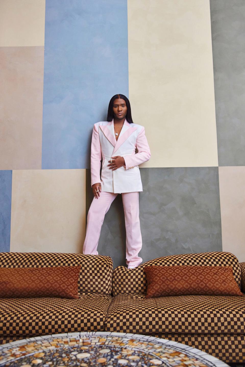 Law Roach standing on couch, pink suit, long straight hair