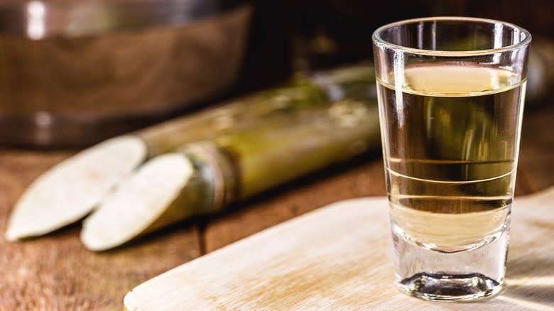 A glass of cachaça next to sugar canes