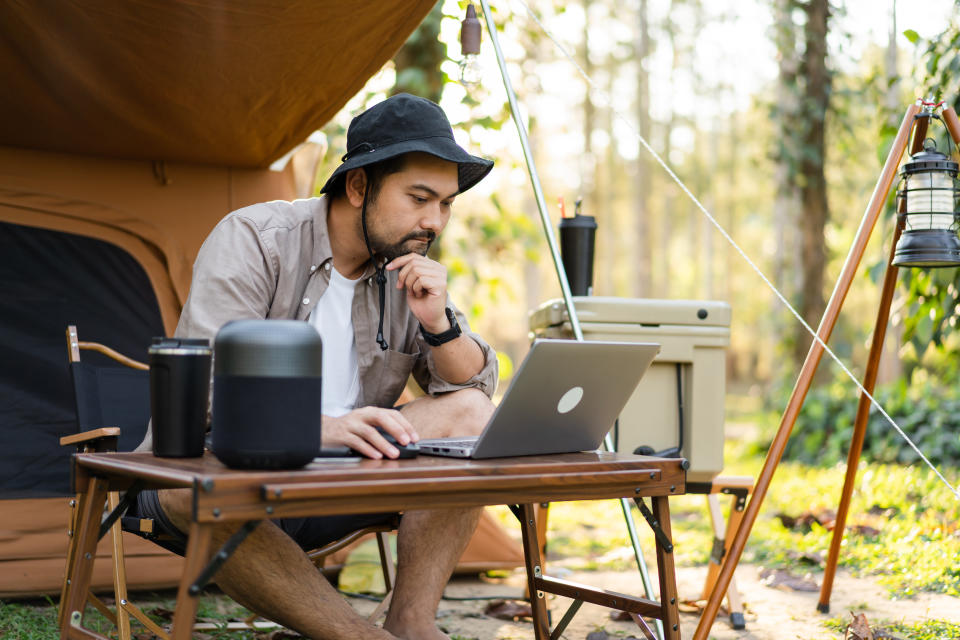 Man enjoys camping sitting in front the camping tent using laptop working remotely