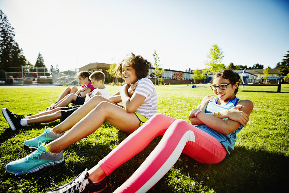 Children sitting on grass in a row doing sit-ups