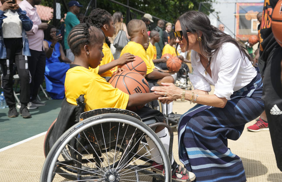 Meghan Markle, right, shake hands with a girl on a wheelchair during the Giant of Africa Foundation at the Dream Big Basketball clinic in Lagos Nigeria, Sunday, May 12, 2024. Prince Harry and his wife Meghan are in Nigeria to champion the Invictus Games, which Prince Harry founded to aid the rehabilitation of wounded and sick servicemembers and veterans. (AP Photo/Sunday Alamba)