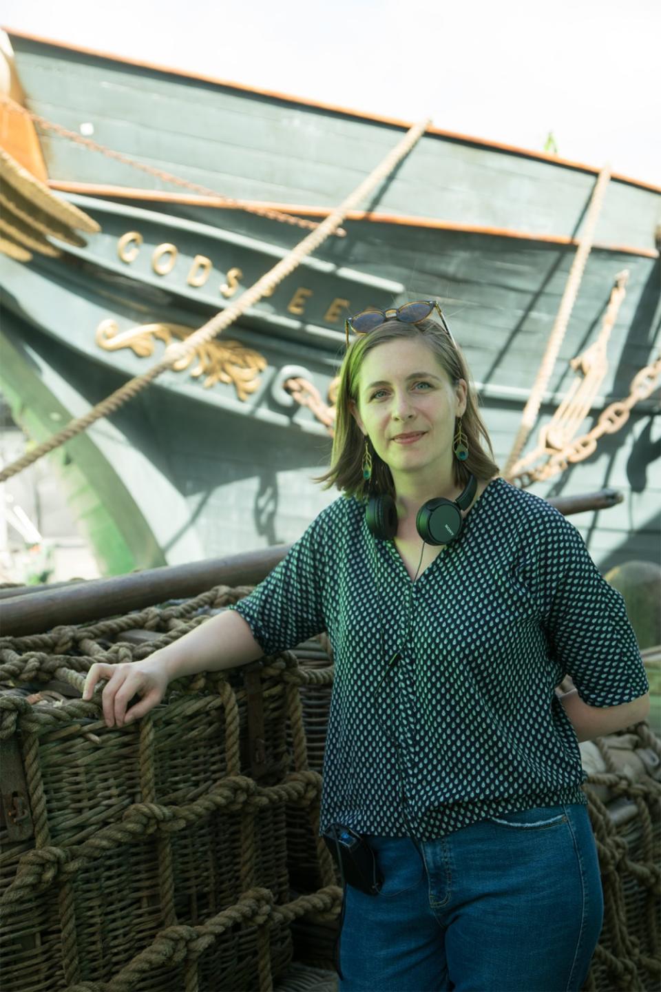 "The Luminaries" author-screenwriter Eleanor Catton standing in front of a blue wooden ship.