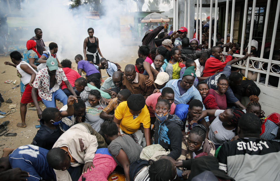 Residents desperate for a planned distribution of food for those suffering under Kenya's coronavirus-related movement restrictions push through a gate and create a stampede, causing police to fire tear gas and leaving several injured, at a district office in the Kibera slum, or informal settlement, of Nairobi, Kenya Friday, April 10, 2020. (AP Photo/Brian Inganga)