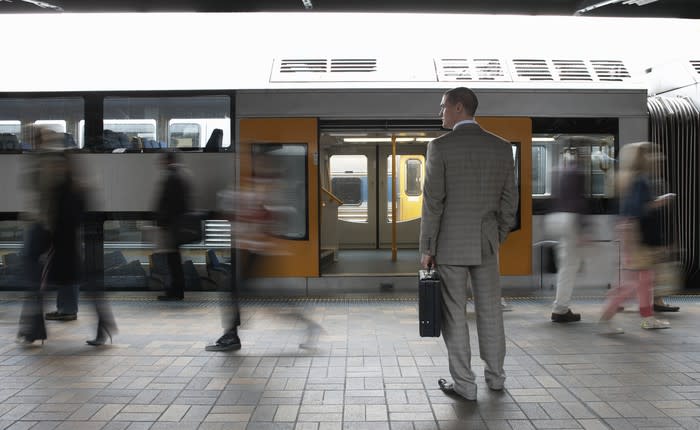 Man in suit on train platform in front of a train with open doors