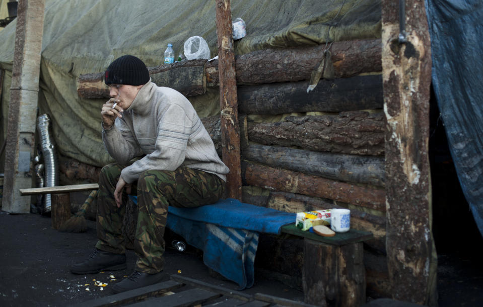 A member of a self defense volunteer group smokes a cigarette as he sits outside a tent in Kiev's Independence Square, Ukraine, Tuesday, March 11, 2014. (AP Photo/David Azia)