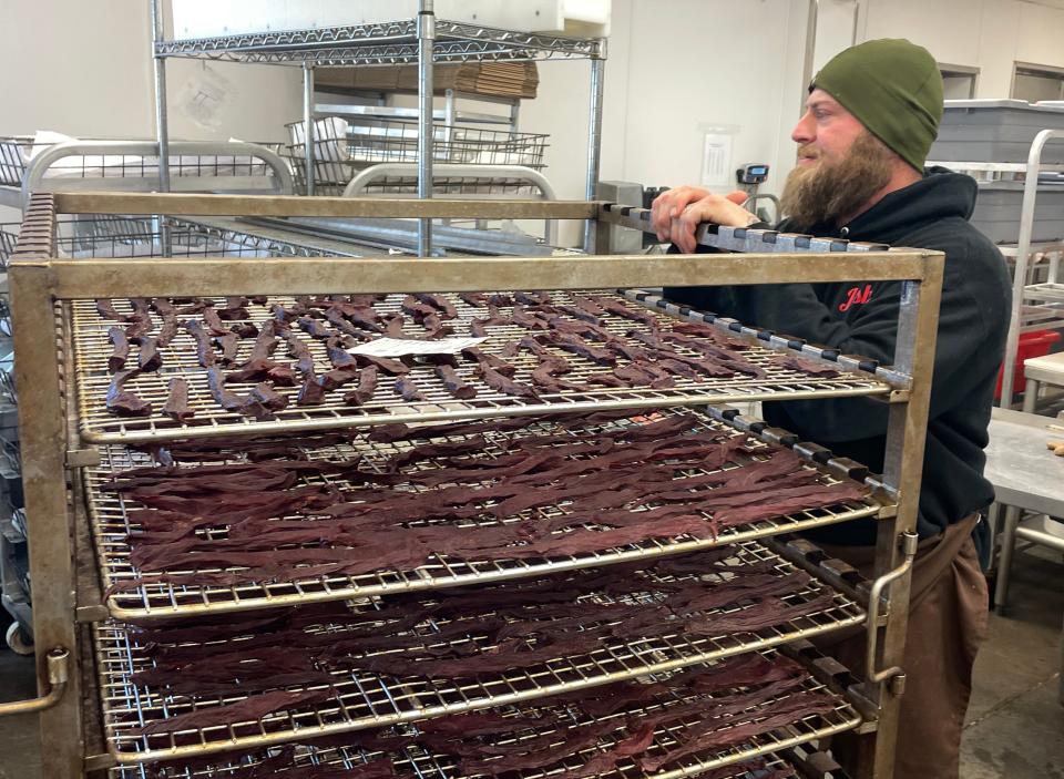 Josh Clark stands near a rack of drying venison jerky as he speaks with coworkers at Cutting Edge Meat Market in Piedmont, S.D.