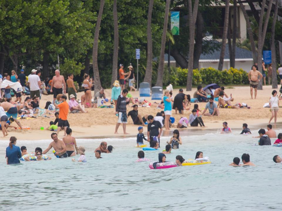 tourists standing in the water and on the sand at the Hilton Hawaiian Village Lagoon in Waikiki, Hawaii