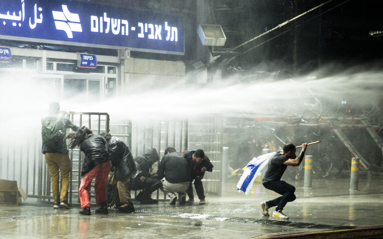 Israeli protesters cower as police use water cannon after clashes erupt during a demonstration against the judicial overhaul - Amir Levy/Getty
