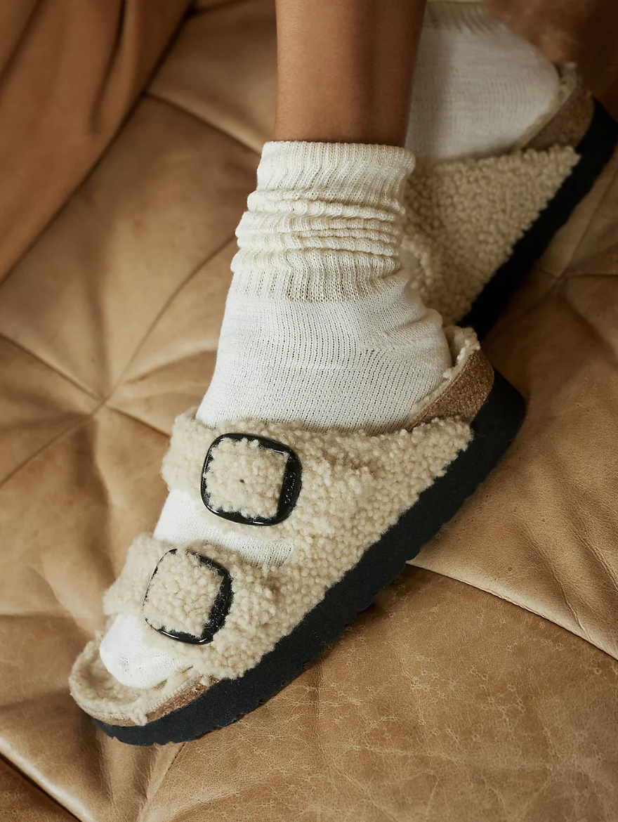 Birkenstock Arizona Teddy Sandals in shearling cream on brown sofa (photo via Anthropologie)