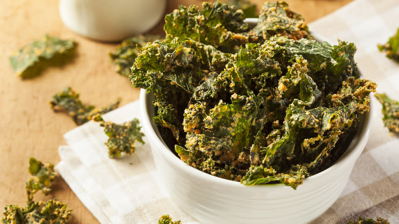 kale chips in white bowl on counter topped with vegan cheese