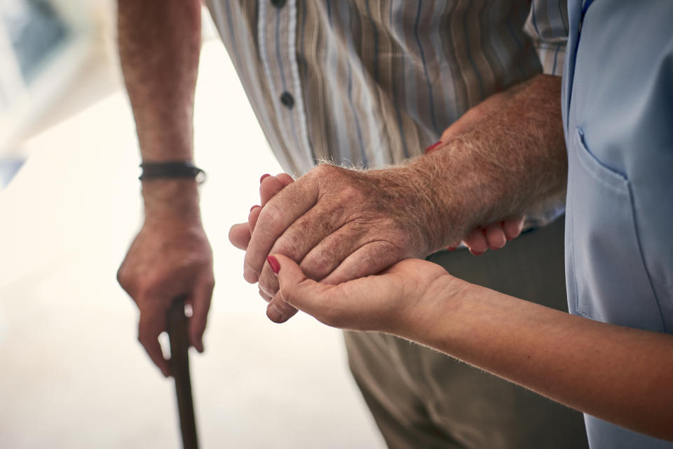 Pictured is an elderly man with a walking stick being helped by an aged care worker. The image is a file image.