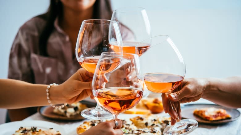 Hands toasting rose wine over dinner table