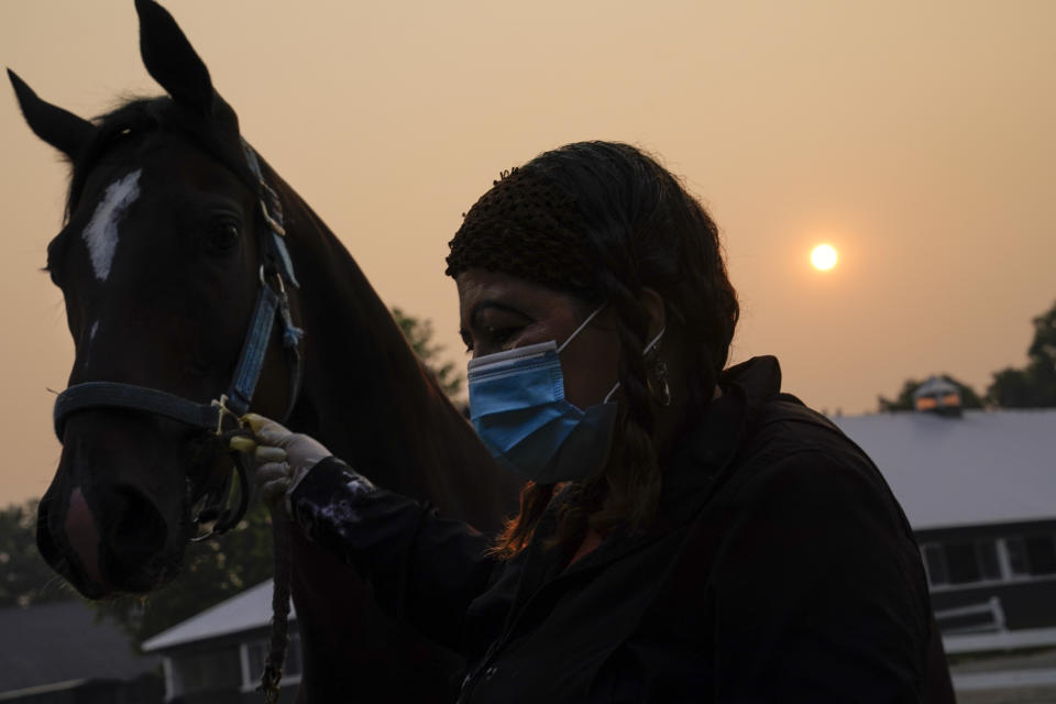 A handler wears a mask as she leads a horse back into the stables as the sun is obscured by haze caused by northern wildfires ahead of the Belmont Stakes horse race, Thursday, June 8, 2023, at Belmont Park in Elmont, N.Y. Training was cancelled for the day due to poor air quality. (AP Photo/John Minchillo)