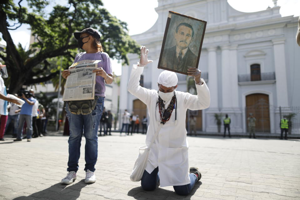 Yeni Vasquez raises a portrait of the late, Venezuelan Dr. Jose Gregorio Hernandez outside the church in La Candelaria after the church bell rang, signaling the start of his Beatification ceremony in Caracas, Venezuela, Friday, April 30, 2021. Known as the "doctor of the poor, Hernandez is being Beatified by the Catholic church, a step towards sainthood. (AP Photo/Ariana Cubillos)