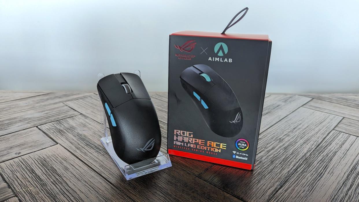 A black ASUS ROG Harpe mouse on a brown wooden table with its packaging.