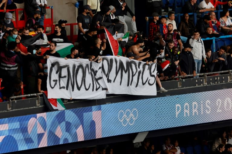 Hinchas muestran una pancarta en la que se lee "Genocide Olympics" y ondean banderas palestinas durante el partido de fútbol entre Israel y Paraguay en los Juegos Olímpicos. En el estadio Parque de los Príncipes de París, el 27 de julio de 2024 (GEOFFROY VAN DER HASSELT)