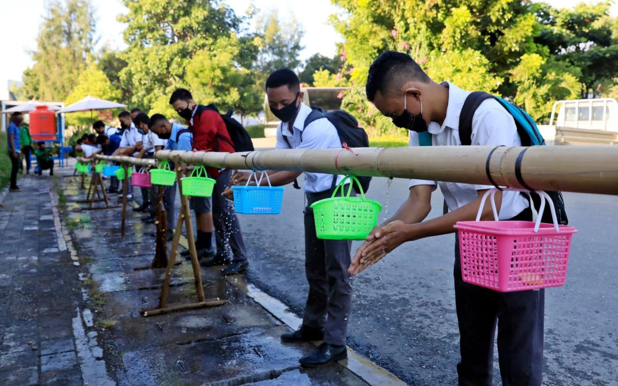 Students wearing protective face masks wash their hands before entering their classes at a reopened private school - Antonio Dasiparu/Shutterstock