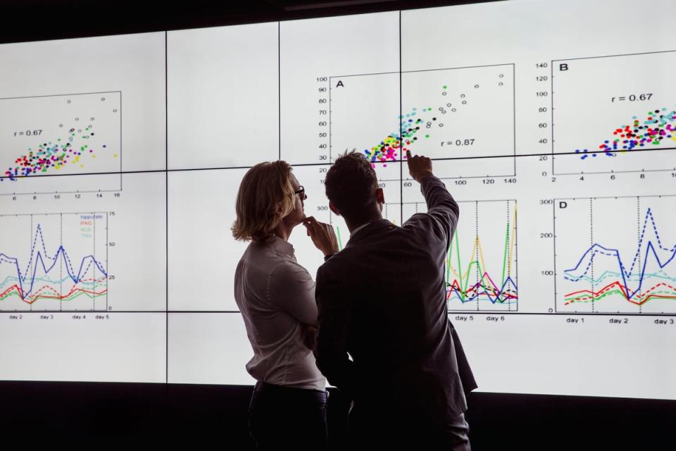 Two people looking at a giant screen with graphs on it.