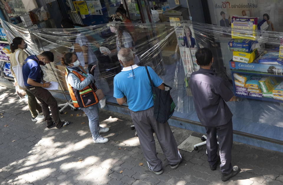 Customers wearing protective masks to help curb the spread of the coronavirus order medicine through plastic sheets front of drug store in Bangkok, Thailand, Thursday, May 27, 2021. (AP Photo/Sakchai Lalit)