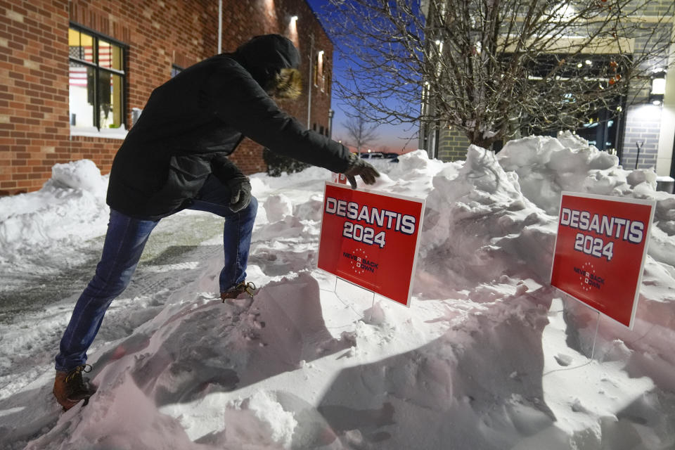 A campaign worker places signs in a snowbank before Republican presidential candidate Florida Gov. Ron DeSantis speaks at a campaign event, Sunday, Jan. 14, 2024, in Ankeny, Iowa. (AP Photo/Charlie Neibergall)