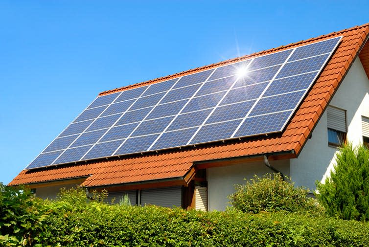 A white-walled house with red-tile roof covered in blue solar panels.