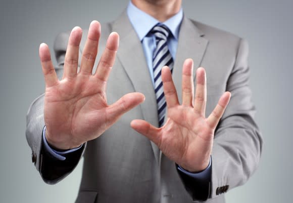 A businessman in a suit putting his hands up as if to say no thanks.