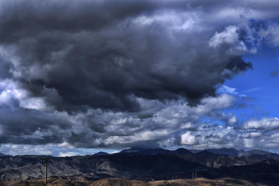 Passing storm clouds move over the mountains in Castaic, Calif., on Wednesday, Nov. 9, 2022. A powerful storm pounded California with rain and snow Tuesday, leaving one person dead and two others missing after they were swept away by floodwaters in a canal, while a tornado touched down in Sacramento County. (AP Photo/Richard Vogel)