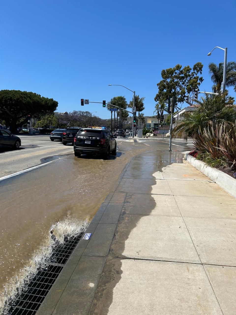 A Ventura police vehicle drives past water rushing into a storm drain on South Mills Road at Dean Drive after a water main break Friday afternoon. City water crews were working on emergency repairs, officials said.