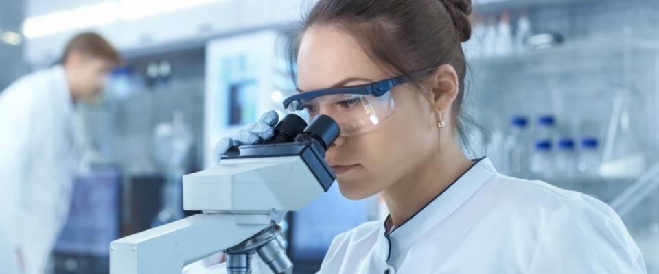 Medical Research Scientists Looking at Samples Under Microscope. She Works in a Bright Modern Laboratory.