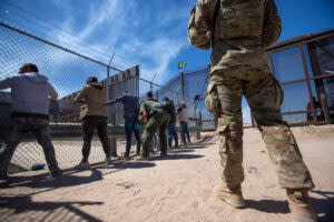 A Texas National Guardsman observes as Border Patrol agents pat down migrants who have surrendered themselves for processing