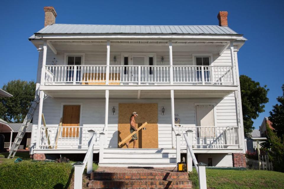 Hurricane preparation man boarding up windows of white historical house