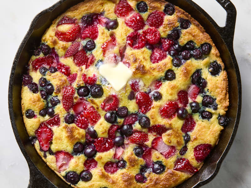 Overhead photo of a mixed berry skillet pancake in a black cast iron skillet topped with butter.