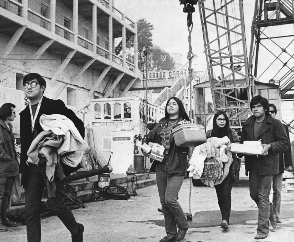 FILE - In this Dec. 2, 1969, file photo, a new group of arrivals walks across the docking area with handfuls of possessions during the Native American occupation of Alcatraz Island in San Francisco. The week of Nov. 18, 2019, marks 50 years since the beginning of a months-long Native American occupation at Alcatraz Island in the San Francisco Bay. The demonstration by dozens of tribal members had lasting effects for tribes, raising awareness of life on and off reservations, galvanizing activists and spurring a shift in federal policy toward self-determination. (AP Photo/RWK, File)