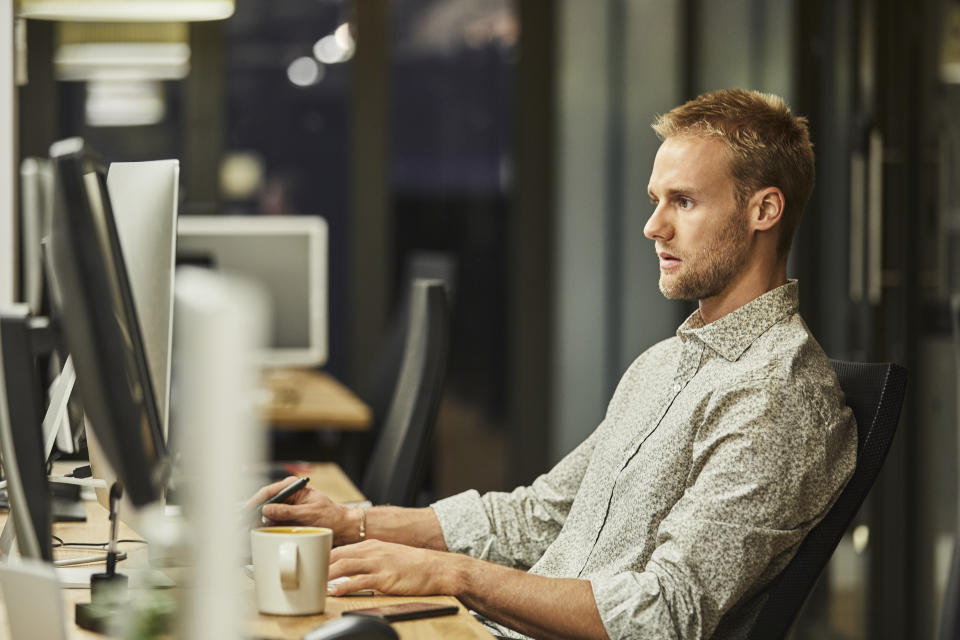 Handsome young businessman using computer. Male entrepreneur is working in creative office. He is sitting at desk.