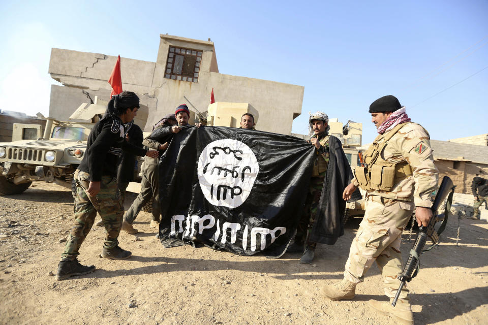 FILE - Iraqi Army soldiers celebrate as they hold a flag of the Islamic State group they captured during a military operation to regain control of a village outside Mosul, Iraq, Nov. 29, 2016. Ten years after the Islamic State group declared its caliphate in large parts of Iraq and Syria, the extremists now control no land, have lost many prominent founding leaders and are mostly away from the world news headlines. (AP Photo/Hadi Mizban, File)