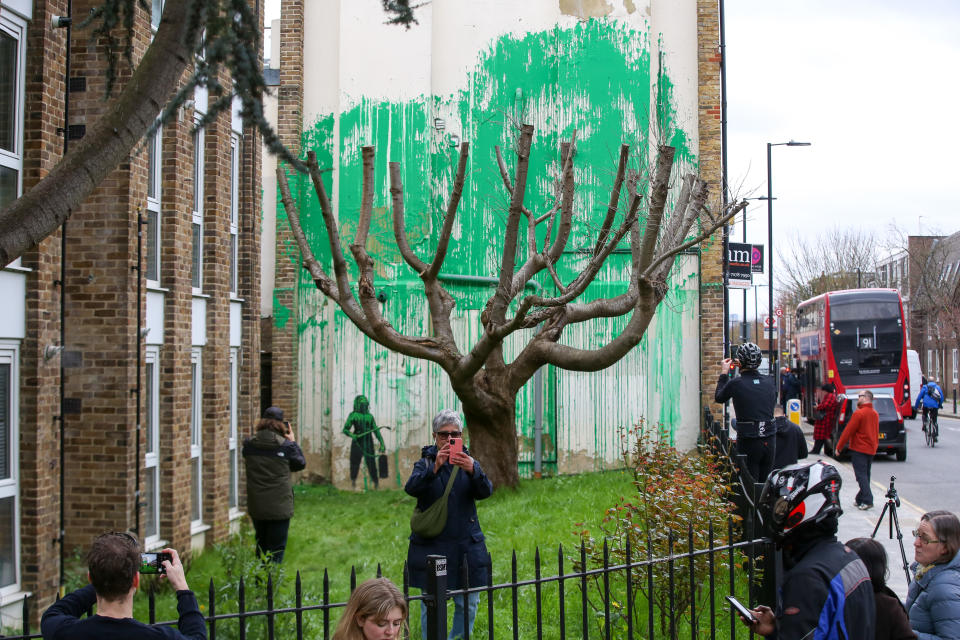 LONDON, UNITED KINGDOM - 2024/03/18: People gather to take photographs of Banksy art in Finsbury Park. The graffitied mural appeared on a wall next to a tree on Hornsey Road in north London. (Photo by Steve Taylor/SOPA Images/LightRocket via Getty Images)