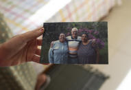 Nazare Rosa de Paula, 67, wife of Geraldo de Paula who died of Covid-19, holds a photo of him embracing two cousins, in their home in Rio de Janeiro, Brazil, Friday, Aug. 7, 2020. Geraldo de Paula, 70, originally from Minas Gerais, moved with his wife more than 40 years ago to Rio where their two children were born. He loved to play the guitar and to make jokes. (AP Photo/Silvia Izquierdo)