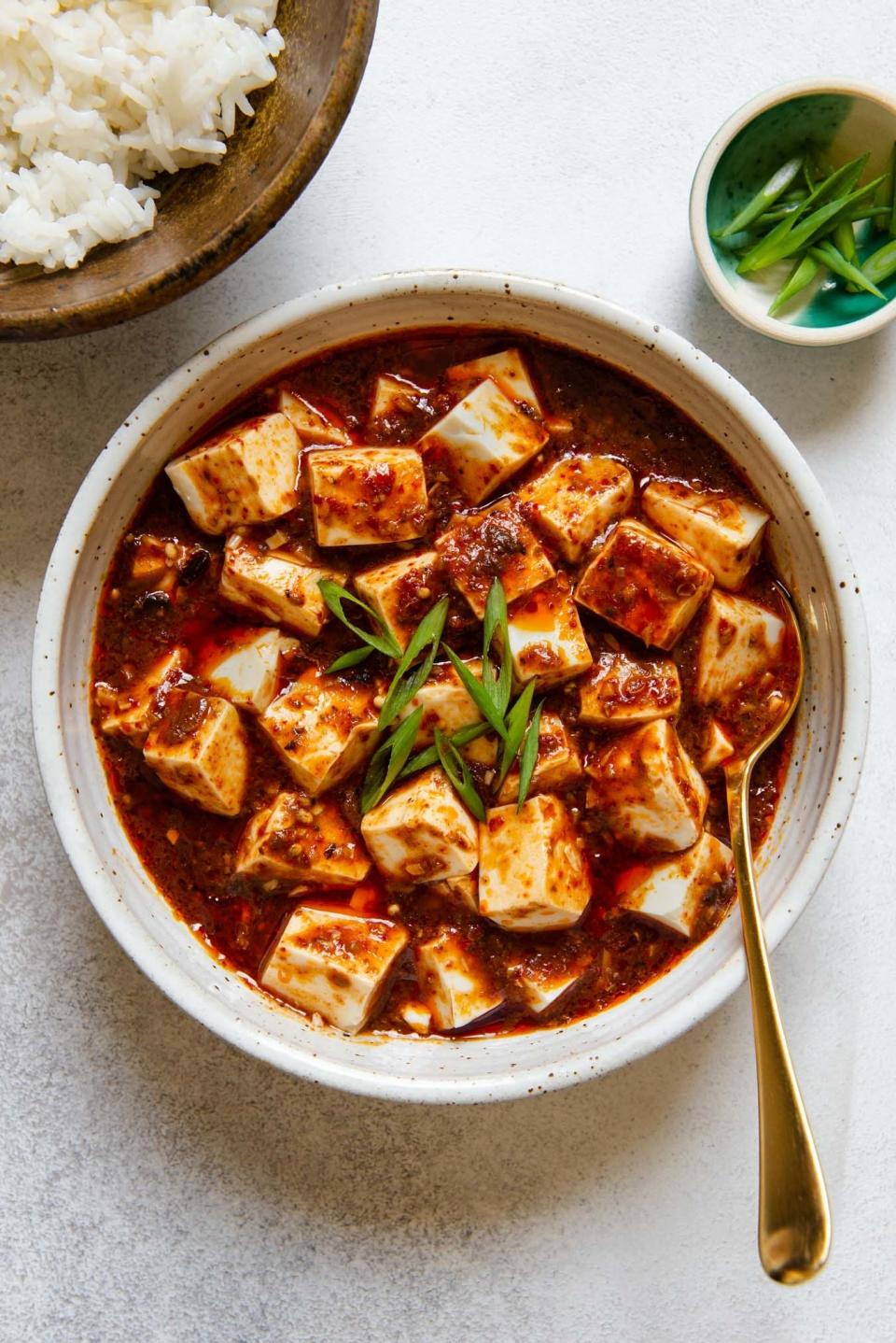 A bowl of tofu cubes in a spicy red sauce with scallions on top