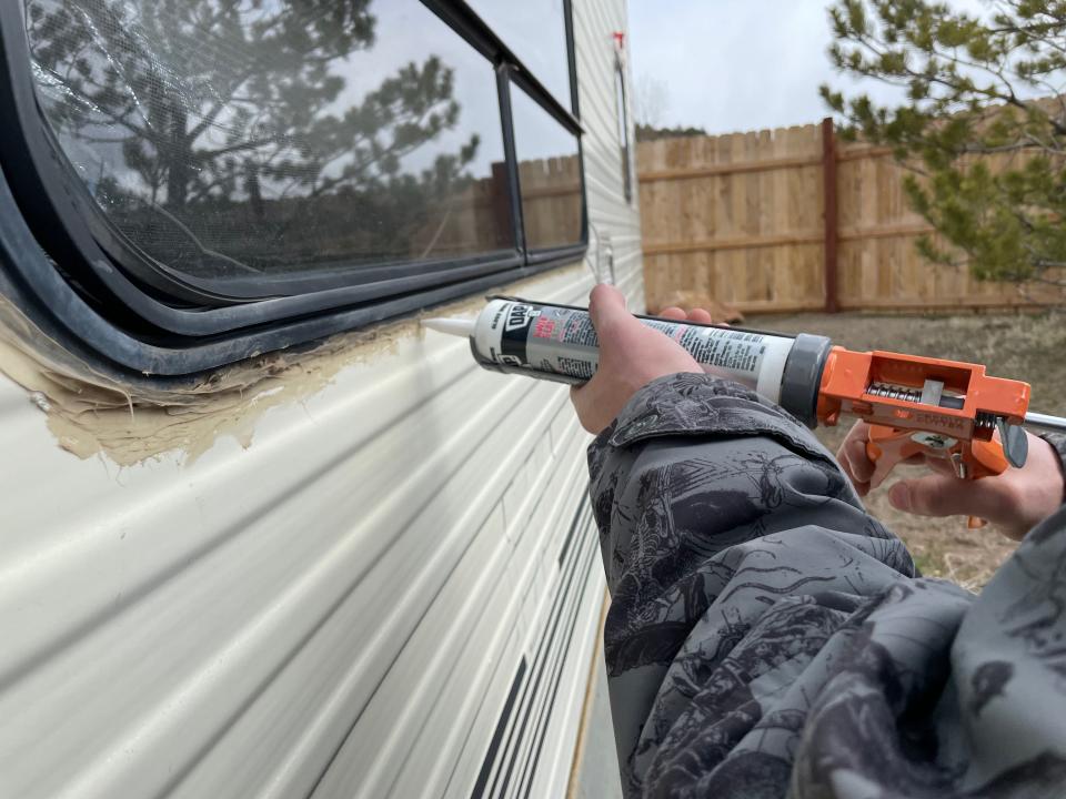 a hand applying caulk to the window of a white van