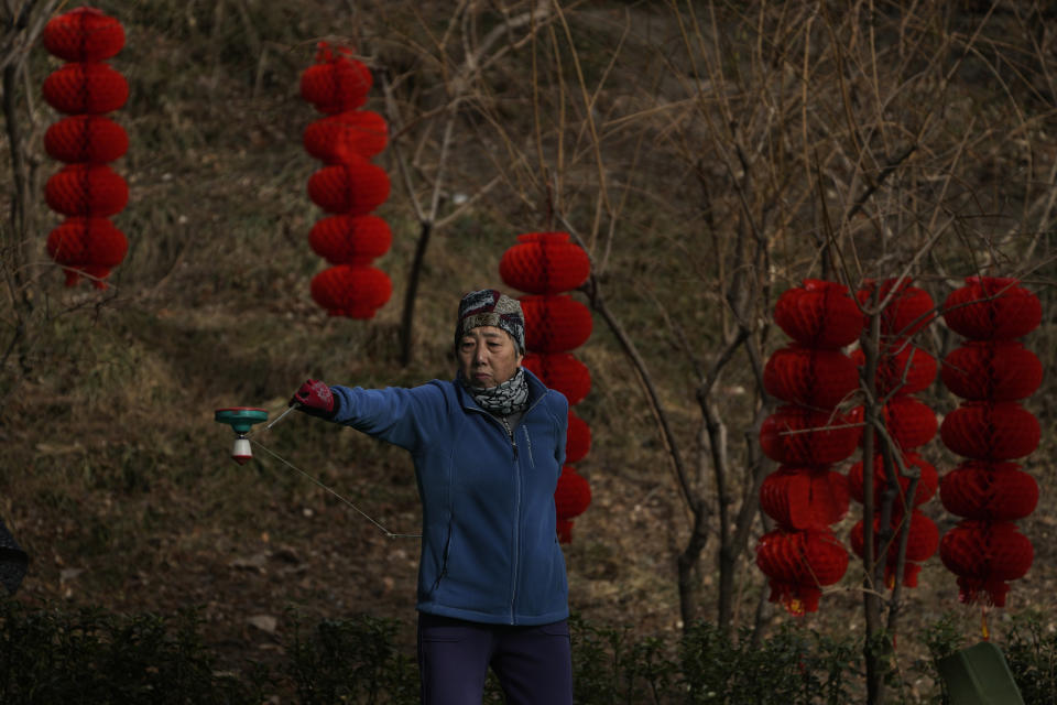 An elderly woman exercises with a spinning top decorated with Lunar New Year decorations in Beijing, Thursday, Jan. 19, 2023. China on Thursday accused "some Western media" of bias, smears and political manipulation in their coverage of China's abrupt ending of its strict "zero-COVID" policy, as it issued a vigorous defense of actions taken to prepare for the change of strategy. (AP Photo/Andy Wong)